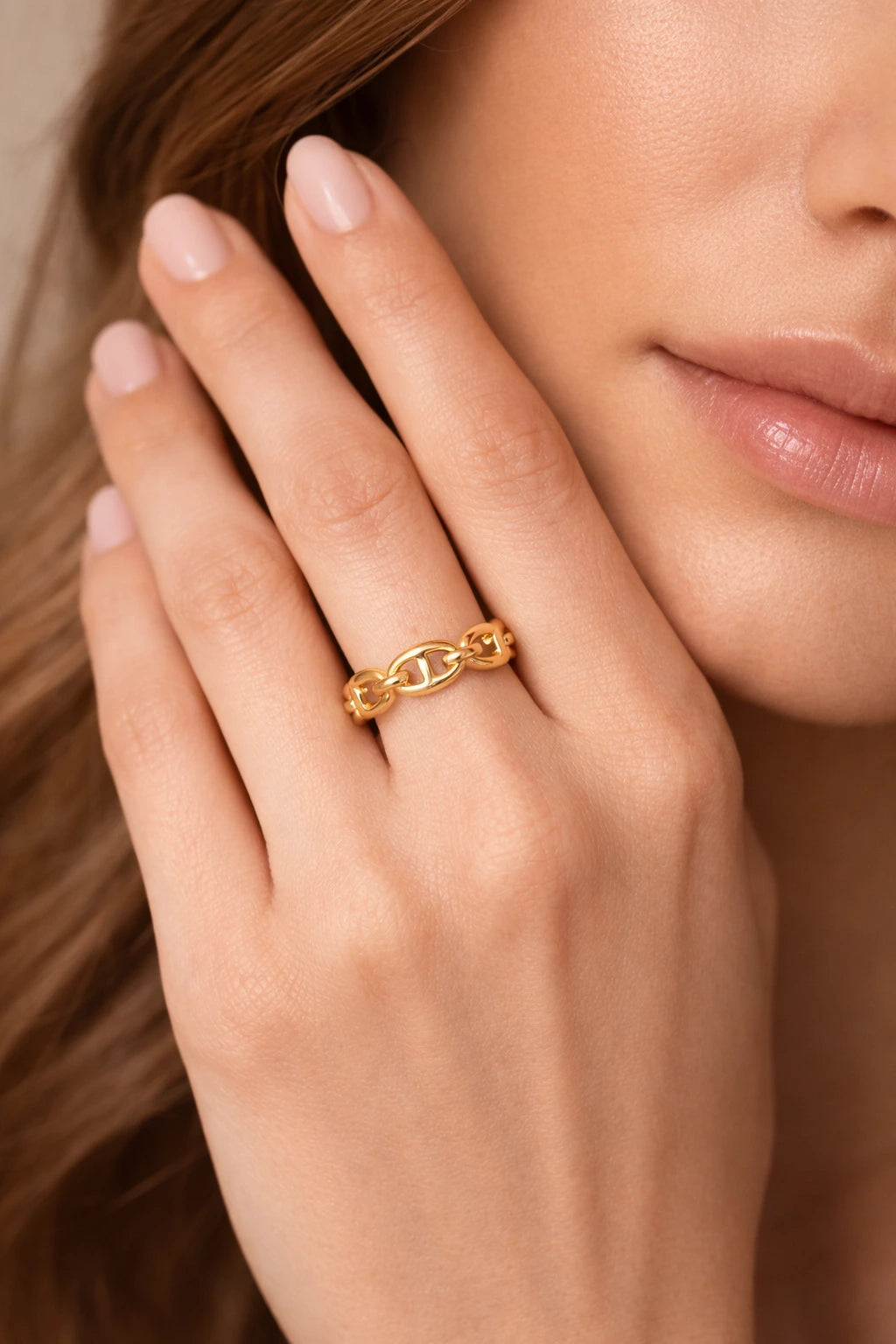 Detailaufnahme eines goldfarbenen Ankerketten-Rings der Marke 'VARALIDA', getragen an der Hand einer Frau vor einem neutralen Hintergrund.