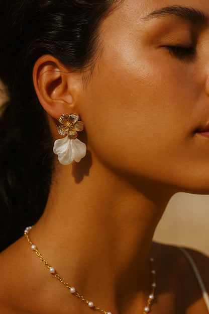 Nahaufnahme des Gesichtsprofils einer jungen Frau mit gebräunter Haut, die gold-weiße Blumenohrringe und eine feine goldene Halskette mit weißen Perlen trägt. Das warme, natürliche Licht betont ihre Hauttextur und die Details des Schmucks vor einem dezenten Hintergrund.